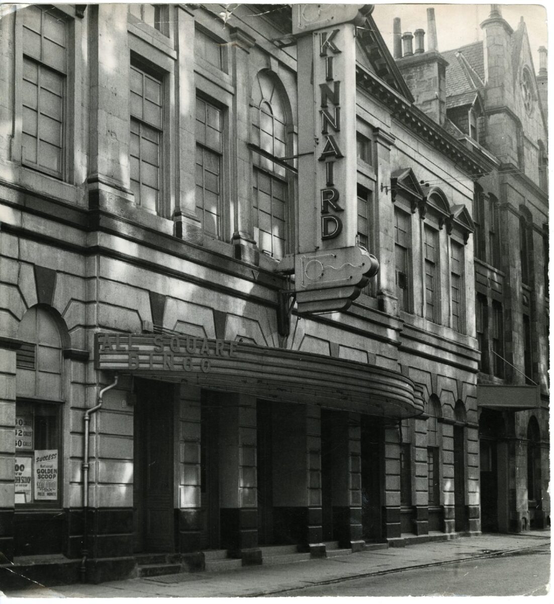 Historic black-and-white photograph of the Kinnaird cinema façade on a quiet city street, featuring a vertical “KINNAIRD” sign above the entrance canopy.