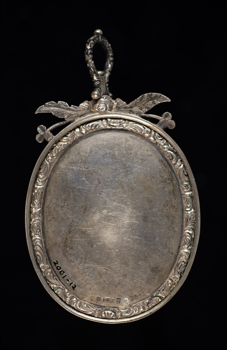 Reverse of an ornate silver presentation medal, featuring a decorative floral border and suspension loop, with a blank central panel showing signs of wear and age.